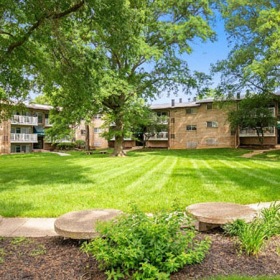 a large green lawn with trees and apartments in the background